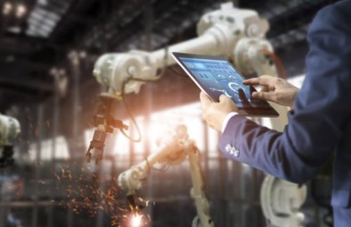 roboty w fabryce i człowiek sterujący nimi z tabletu